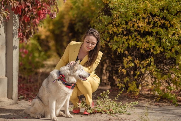 La niña es hermosa en el otoño, con ropa elegante a la moda. Con un perro grande.