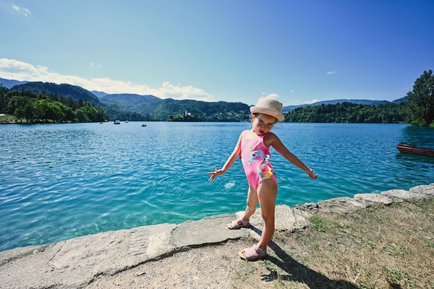 La niña es traje de baño y sombrero planteados en el muelle de vista hermoso lago Bled Eslovenia