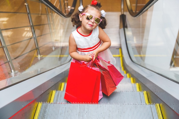 niña en la escalera mecánica en el centro comercial con compras