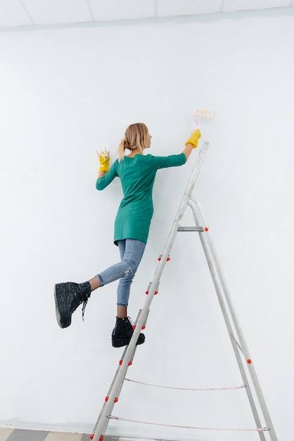 Una niña en una escalera pinta una pared blanca con un rodillo. Reparación del interior.