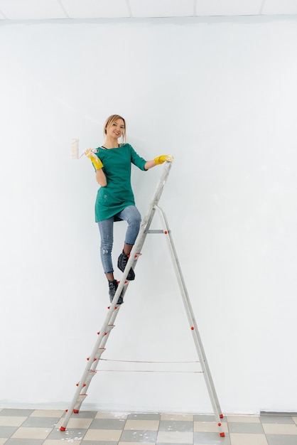 Una niña en las escaleras pinta una pared blanca con un rodillo. Reparación del interior.