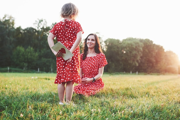 Niña esconde el libro con corazón rojo en la parte posterior de la madre sentada sonriente