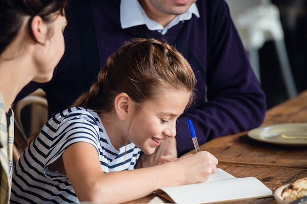 Una niña escribiendo algo en su cuaderno y sonriendo