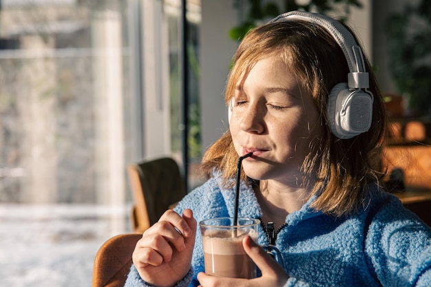 Niña escucha música en auriculares y bebe cacao con mañana soleada