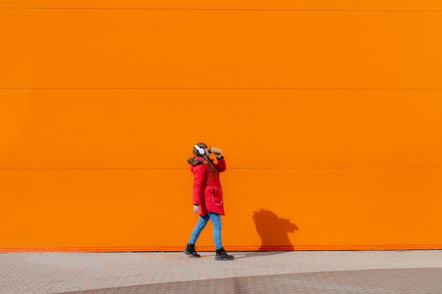 Una niña escucha música con auriculares en el fondo de una pared naranja Espacio de copia Mockup Un artículo sobre la juventud moderna Un artículo sobre música moderna Artículo sobre la elección de auriculares