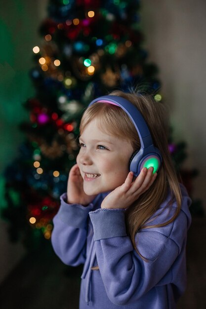 Foto una niña escucha música con auriculares frente a un árbol de navidad con un traje morado.