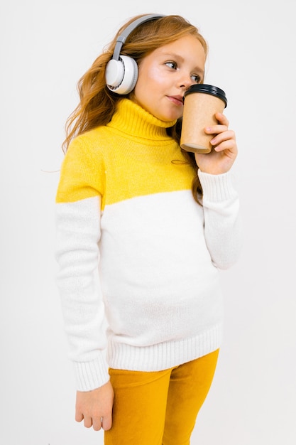 Niña escucha música en auriculares grandes y bebe café