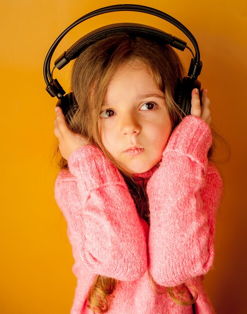 Niña escucha música con auriculares sobre un fondo amarillo