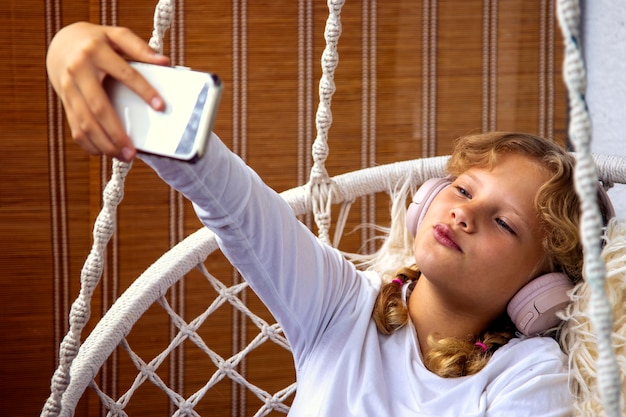 Niña escuchando música con auriculares en su teléfono móvil y tomando un selfie