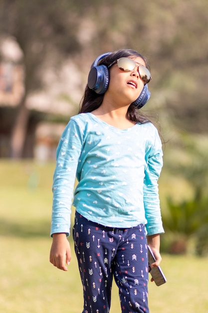 Niña escuchando música en el teléfono inteligente con sus auriculares en el parque