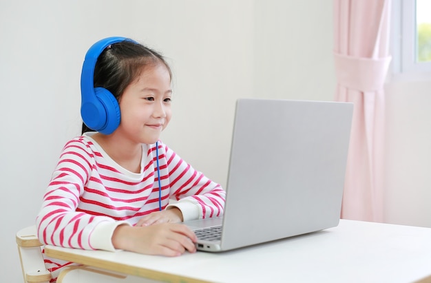 Niña de la escuela asiática que usa la clase de aprendizaje en línea de estudio de auriculares