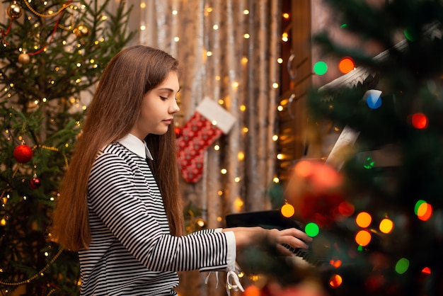 Niña de la escuela concentrada tocando la canción de Navidad en un viejo piano