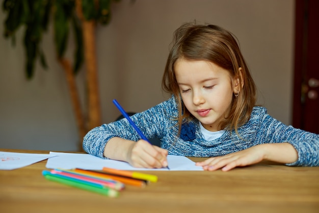 Niña de la escuela dibujando y escribiendo una imagen con crayones, usando lápices de colores