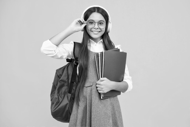 Niña de la escuela estudiante adolescente en auriculares sostiene libros sobre fondo de estudio aislado amarillo Concepto de educación escolar y musical Cara feliz emociones positivas y sonrientes de niña adolescente