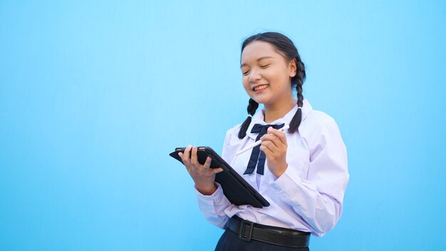 Niña de la escuela feliz con ordenador portátil sobre fondo azul