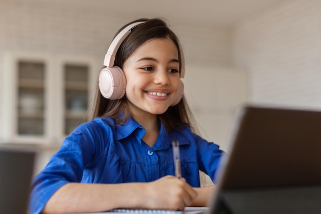 Niña de la escuela feliz usando una computadora portátil viendo una conferencia virtual en casa