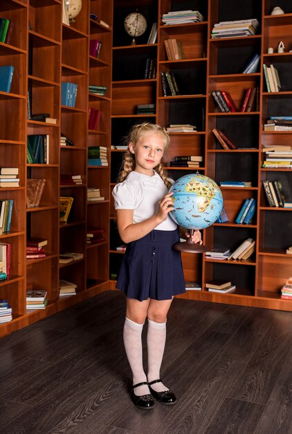 Niña de la escuela inteligente en uniforme se encuentra con un globo en la biblioteca de la escuela