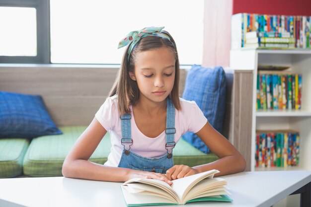 Niña de la escuela leyendo un libro en la biblioteca