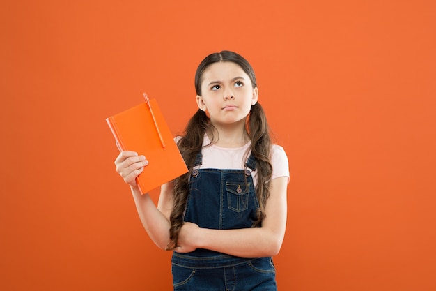 Niña de la escuela leyó el libro sobre fondo naranja. escribir notas.