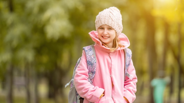 Niña de la escuela con mochila sonriendo en el parque de otoño y mirando a la cámara retrato de niño preadolescente en str