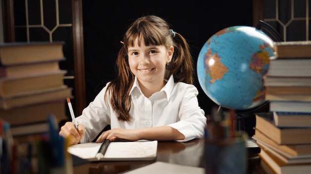 Niña de escuela pensativa de ocho años que estudia el lugar de la mesa de proceso con libros y concepto de educación global