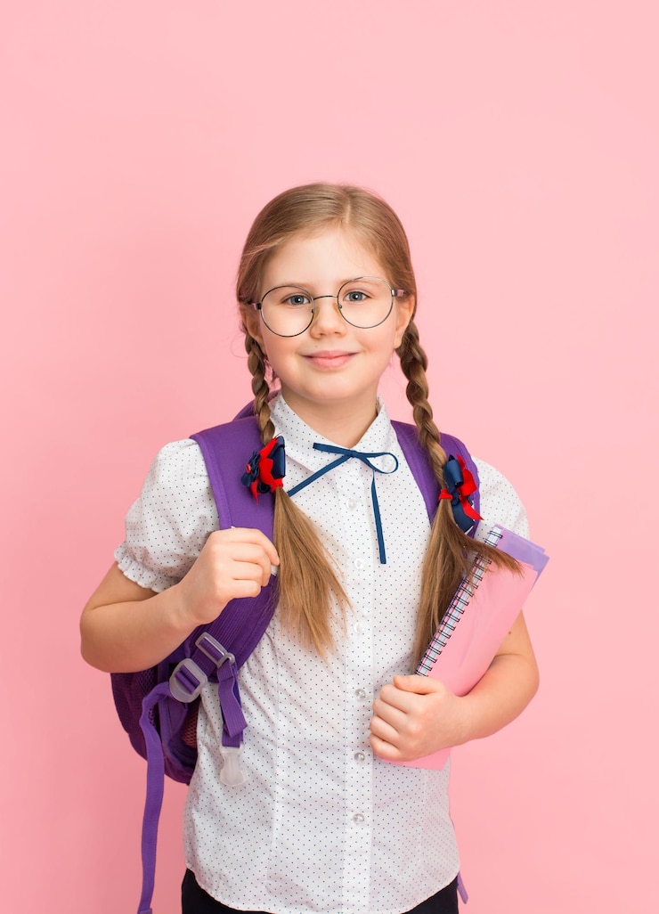Foto niña de escuela positiva con gafas y mochila sonriendo sobre un fondo rosa