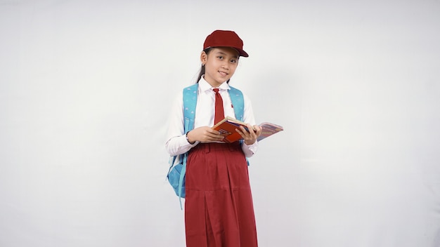 Niña de la escuela primaria asiática libro de apertura sonriendo aislado sobre fondo blanco.