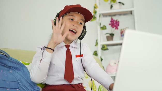 Niña de la escuela primaria asiática que aprende saludo en línea a la pantalla del portátil en casa