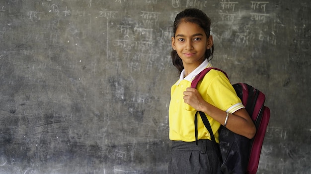 Niña de escuela rural india sonriente con mochila mirando a la cámara