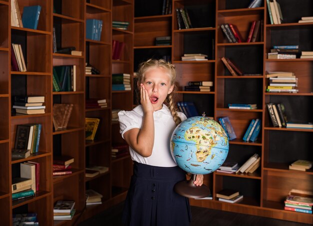 Niña de la escuela sorprendida en uniforme escolar con un globo en la biblioteca