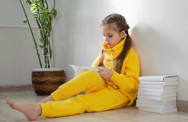 Foto niña de escuela con traje amarillo sentada en el suelo y estudiando un libro concepto de educación estudio tarea estilo de vida escuela primaria y educación para niños niño lee un libro en casa