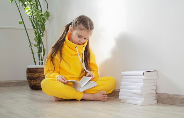 Foto niña de escuela con traje amarillo sentada en el suelo y estudiando un libro concepto de educación estudio tarea estilo de vida escuela primaria y educación para niños niño lee un libro en casa