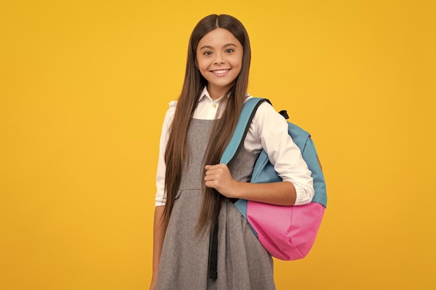 Niña de la escuela en uniforme escolar con mochila escolar Adolescente escolar sostiene mochila sobre fondo amarillo aislado Niña feliz cara emociones positivas y sonrientes