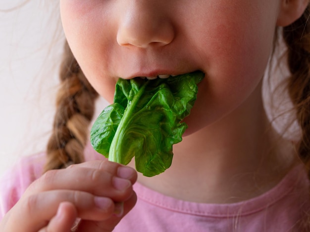 Niña con espinacas frescas en la mano fondo blanco Niño come comida natural Hoja vegetal vitamina vegetariana vegana