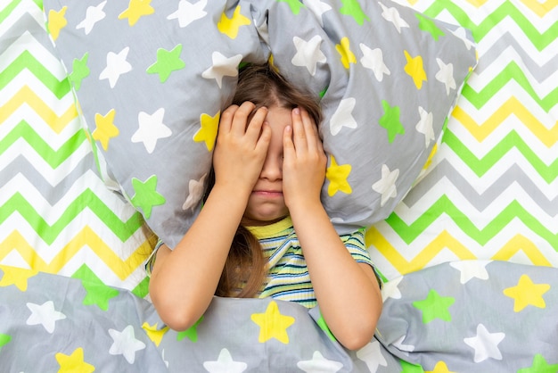 Una niña está acostada en la cama y es traviesa, llora y no quiere levantarse, ir a la escuela.