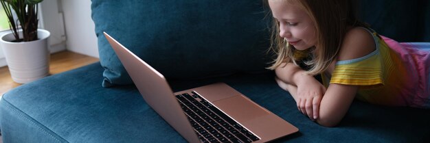 Una niña está acostada en el sofá con una computadora portátil