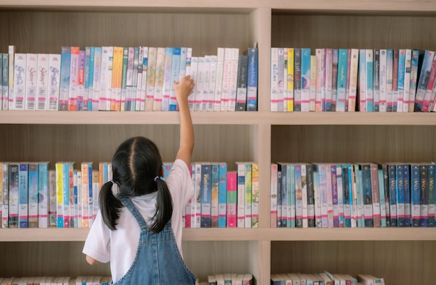 Una niña está alcanzando un libro en una estantería de la biblioteca