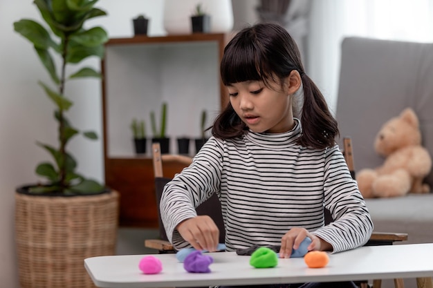 La niña está aprendiendo a usar plastilina de colores en una habitación bien iluminada