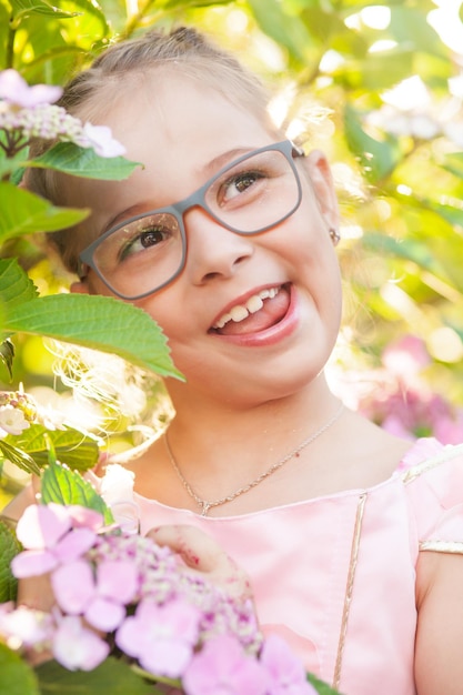 La niña está en arbustos de flores de hortensias en el jardín al atardecer.