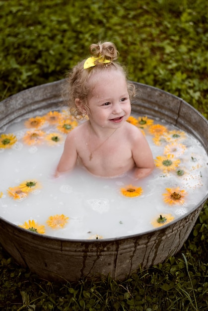 una niña se está bañando en un baño de hierro. el niño se lava y sonríe. una niña en la leche