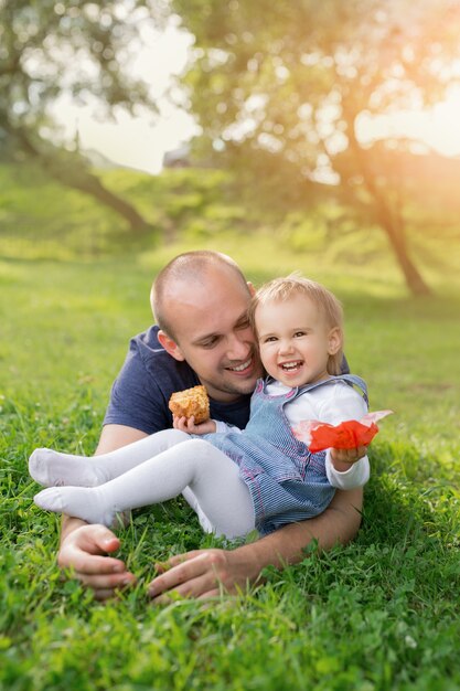 Una niña está comiendo un pastel en los brazos de su padre y riendo alegremente