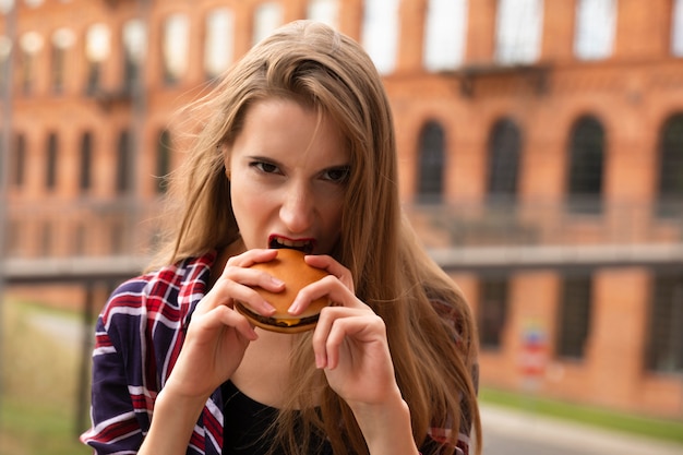 Una niña está comiendo su hamburguesa en la calle. Tiene mucha hambre, despertó en ella un apetito brutal.
