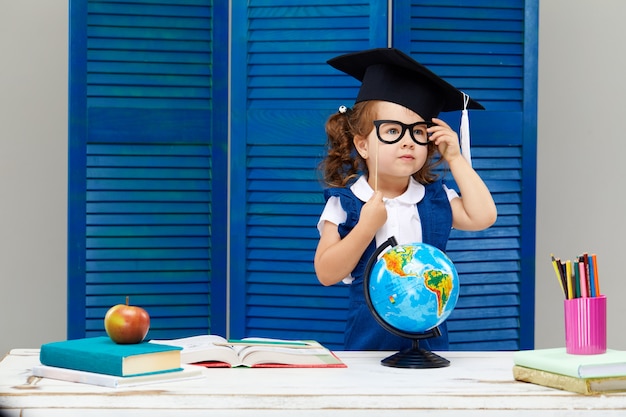 La niña está estudiando mientras usa un gorro de graduación