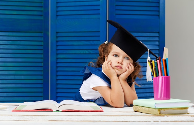 La niña está estudiando mientras usa un gorro de graduación