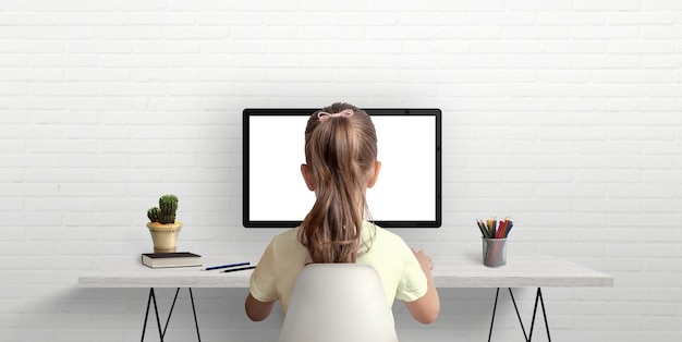 La niña está estudiando y trabajando en la computadora El concepto de usar tecnologías modernas para niños Escritorio de trabajo en la habitación con libros y bolígrafos