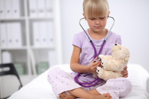 La niña está examinando a su osito de peluche con un estetoscopio