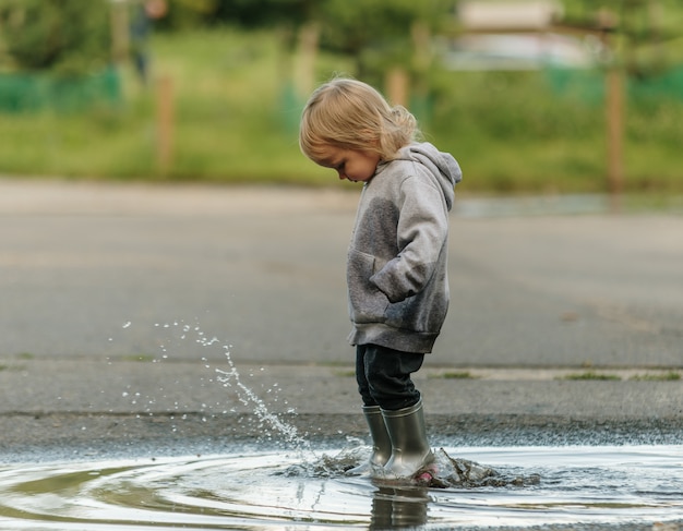 La niña está jugando en el charco con botas de goma.