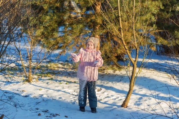 Niña está jugando con nieve en el bosque de invierno. Infancia feliz. Concepto de vacaciones de diversión de invierno