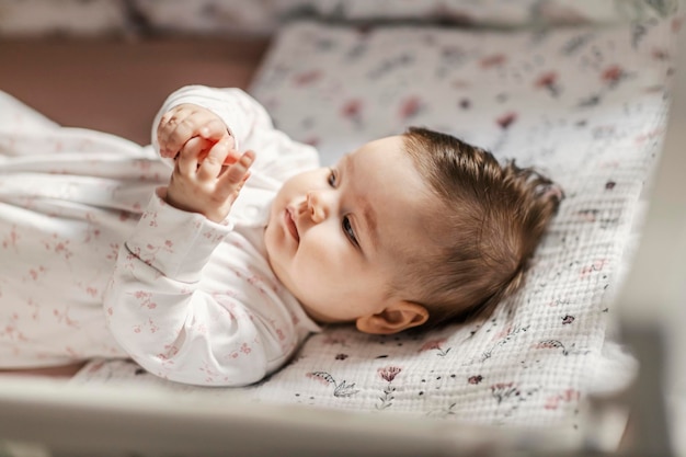 Una niña está jugando con sus dedos mientras está acostada en una cuna