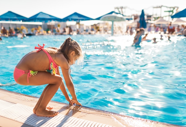 Niña está junto a la piscina y prueba el agua con las manos